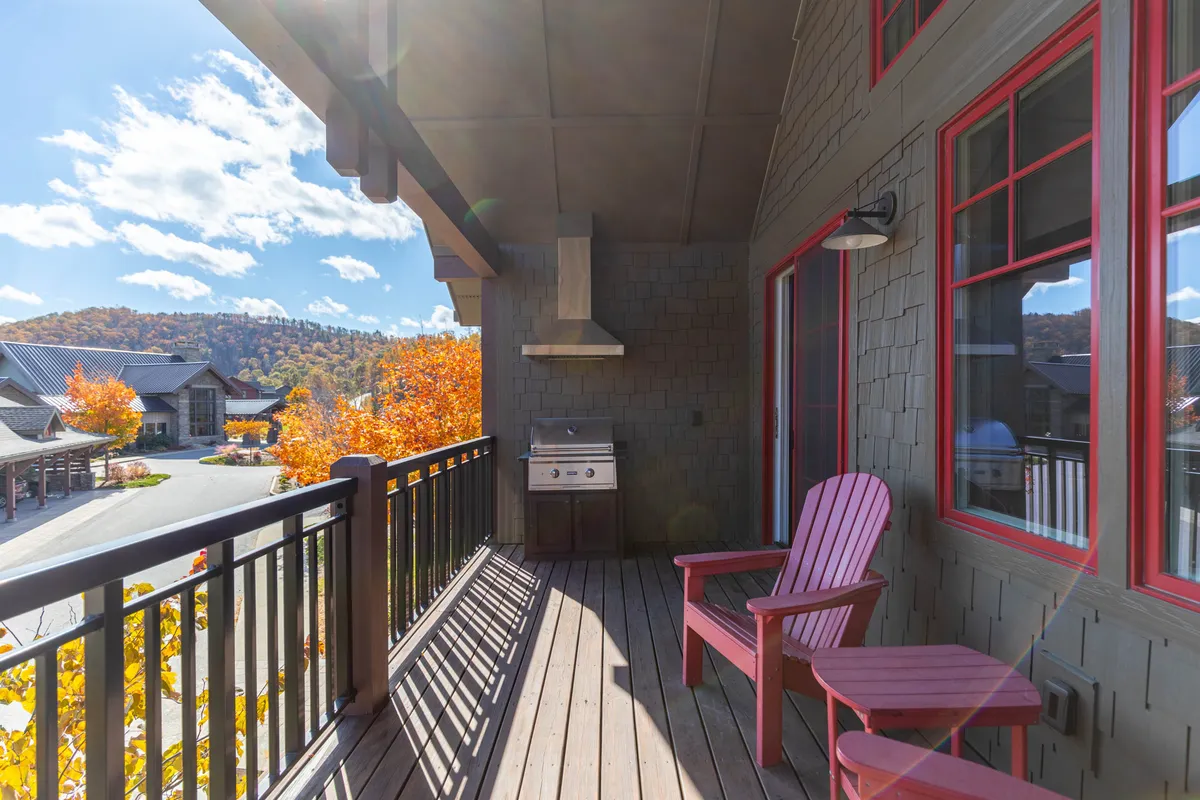 A cozy deck with red chairs and a grill, set against a scenic backdrop. The outdoor seating invites guests to enjoy nature, while the presence of the grill hints at social gatherings or meals with a view of the mountains.