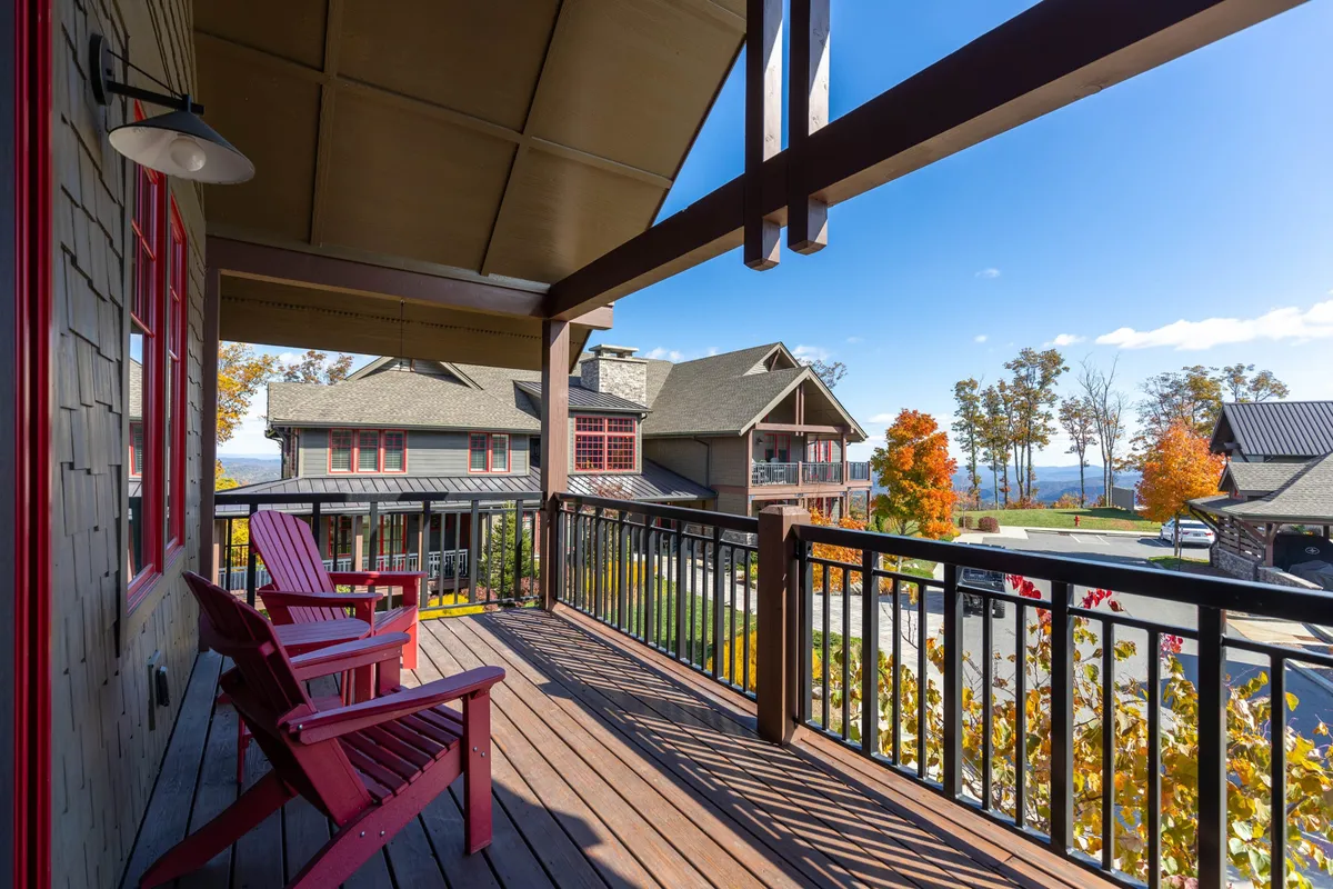 A serene outdoor deck area featuring red Adirondack chairs arranged to face a scenic landscape. The wooden railing frames a sweeping view of lush greenery and mountains beyond, creating an inviting space for relaxation, conversation, and soaking in the natural beauty.