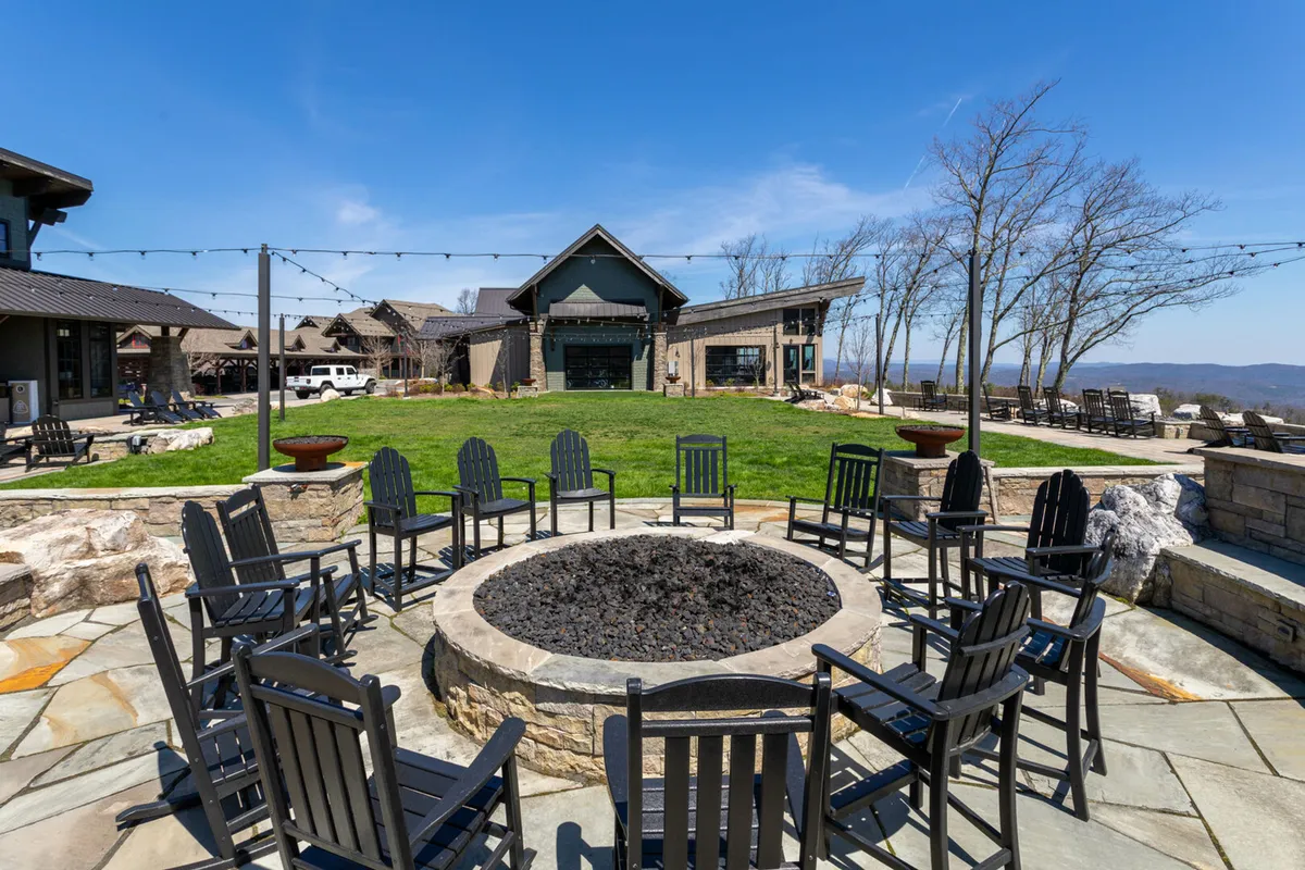 An outdoor fire pit area set on a lush lawn, surrounded by comfortable chairs and decorative lighting. The space is perfect for evening gatherings, socializing, and enjoying the outdoors in a relaxed, communal setting.