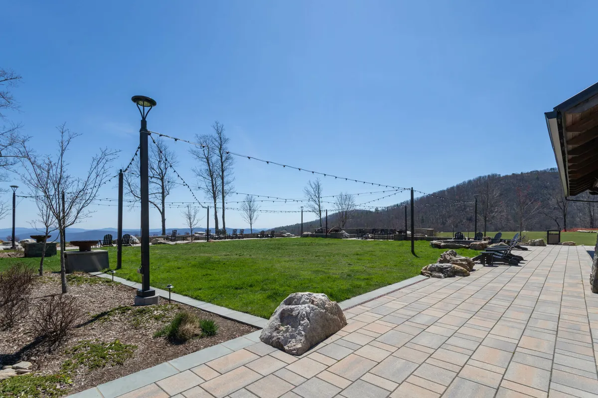 A welcoming green lawn bordered by patio seating, set under string lights, with a stunning mountain view as the backdrop. The scene is designed for outdoor gatherings or intimate moments, enhanced by the soft glow of sunset and the promise of starlit evenings.