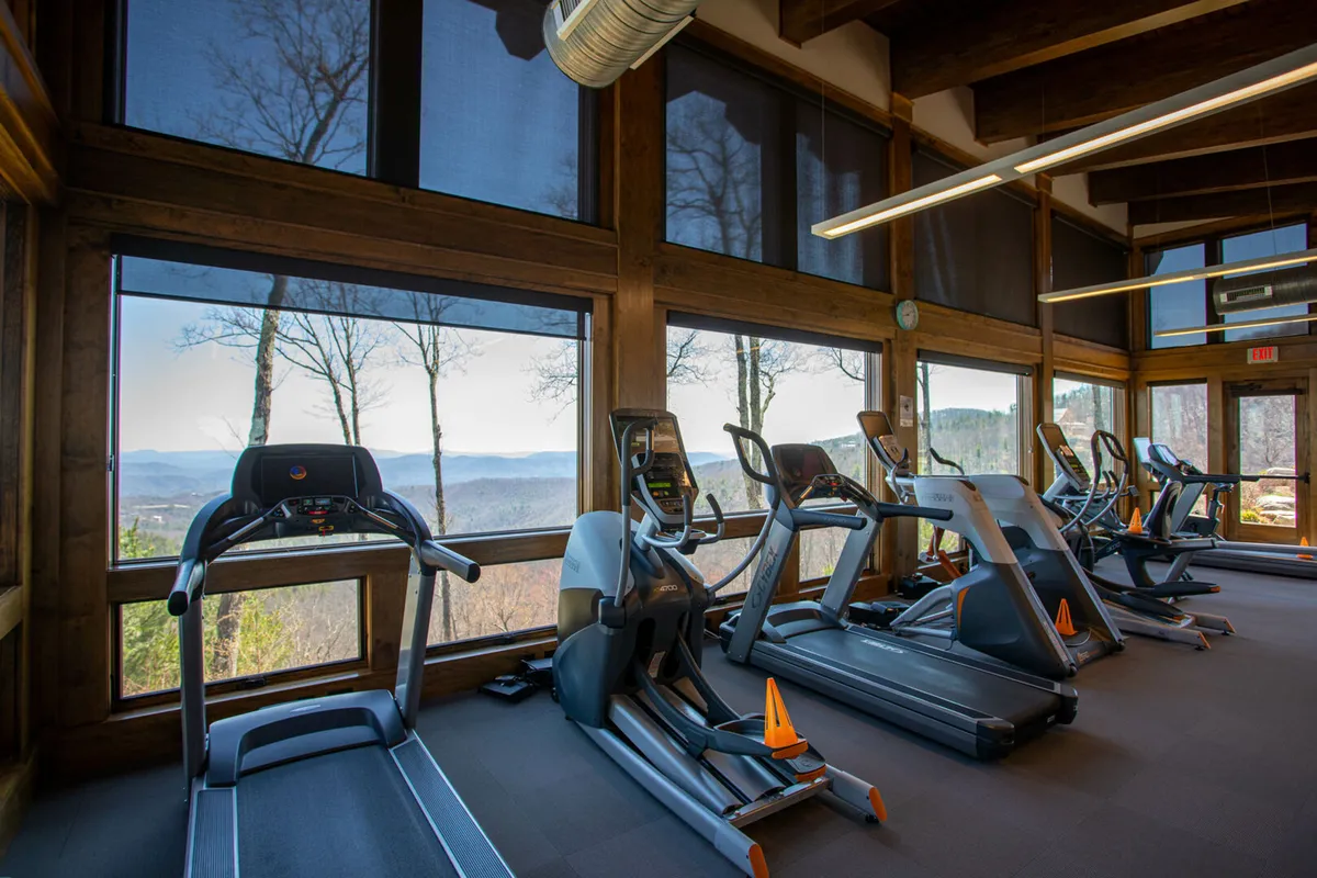 A sunlit fitness center with treadmills facing large windows, offering scenic views of the outdoors. The space is bright and motivational, providing a welcoming environment for shared wellness routines or solo workouts.