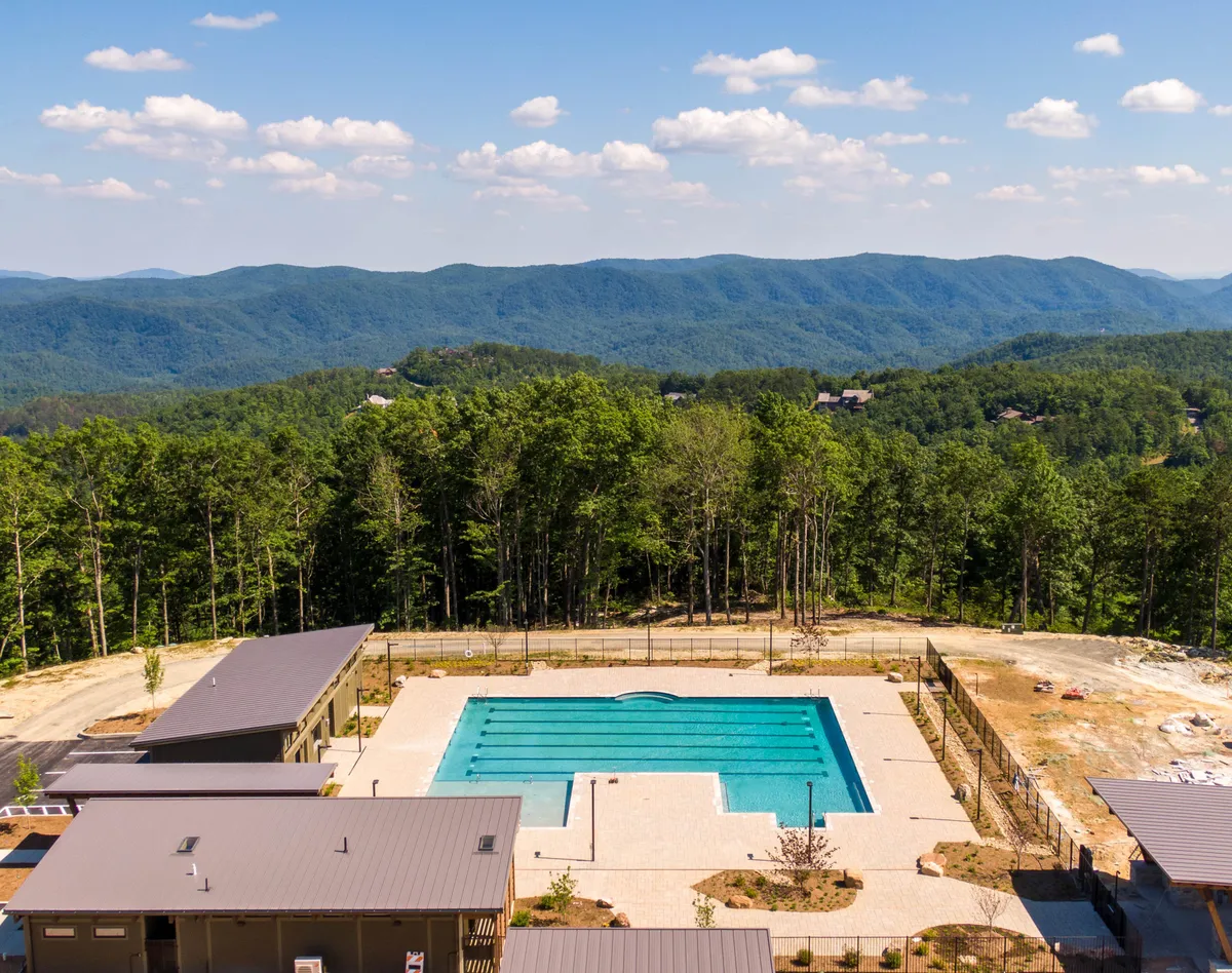 The image showcases a swimming pool set against a stunning mountain backdrop, surrounded by trees. The pool area is designed for swimming, sunbathing, and outdoor gatherings, embodying the leisure and active lifestyle described in the section.