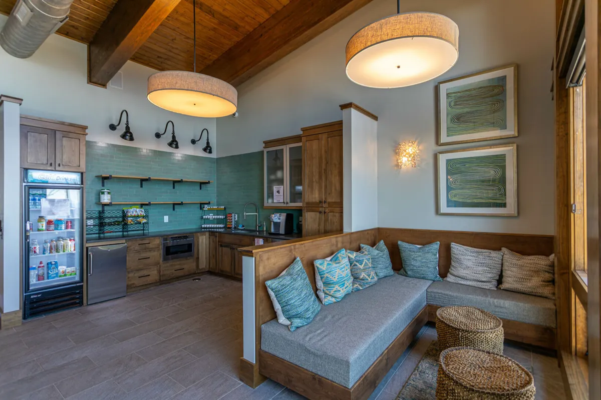 A cozy open-concept living area featuring a kitchen counter, comfortable sofa seating, a refrigerator, wall artwork, and stylish lighting. The setup encourages both cooking and socializing, offering a welcoming space for relaxed gatherings.