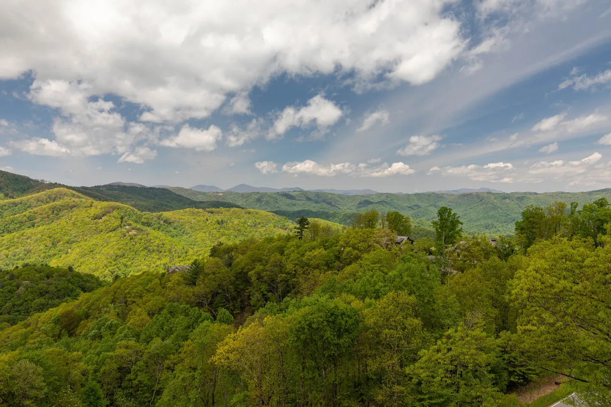 A breathtaking sunrise view over lush green mountains and rolling hills beneath a cloudy blue sky. The tranquil landscape invites outdoor activities like hiking and provides a sense of peace and inspiration.